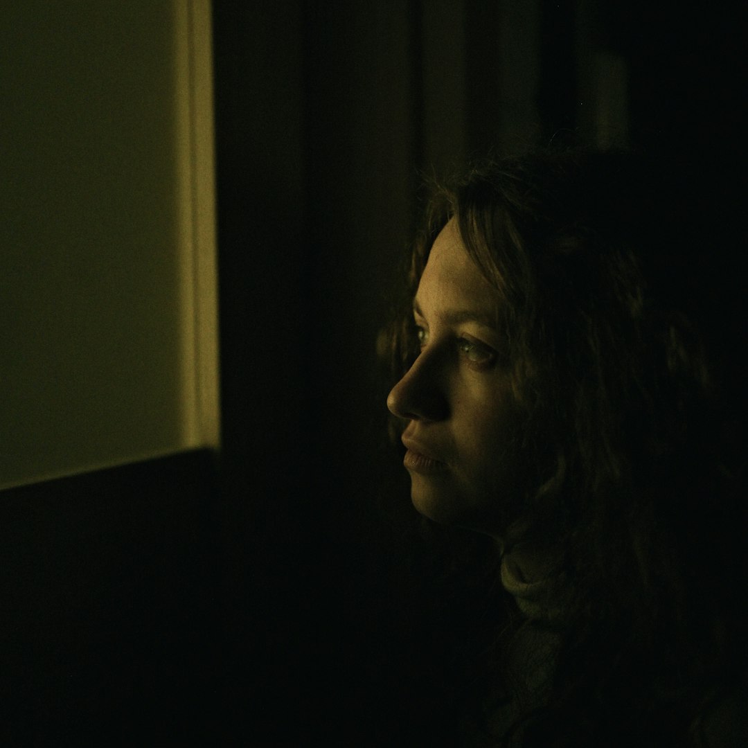 insomnia sleep disorders — Young woman looking out a window in dim light